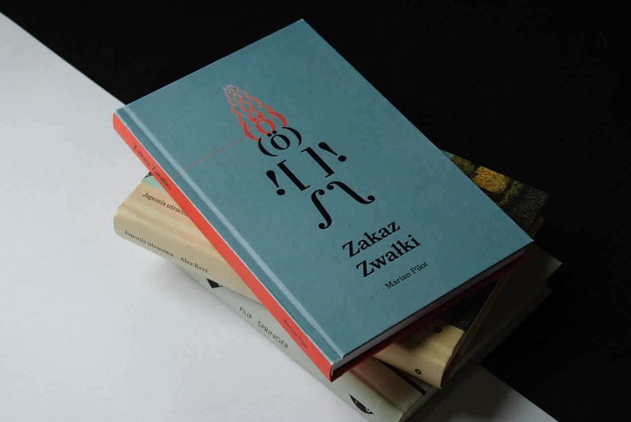 Hardcover book “Zakaz Zwałki” with a teal cover and red illustration, lying on a stack of books